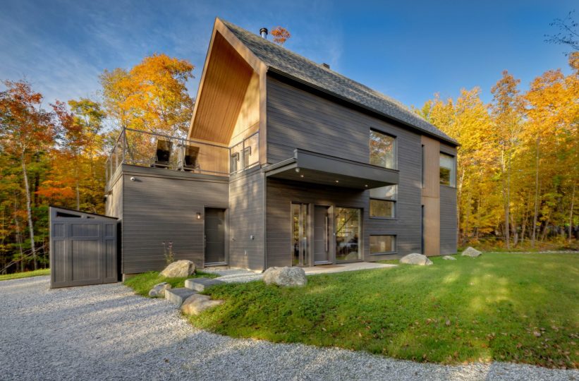 Maison scandinave sur dalle à 2 niveaux vue de l&#039;extérieur. Revêtement extérieur gris et bois naturel, terrasse sur le garage
