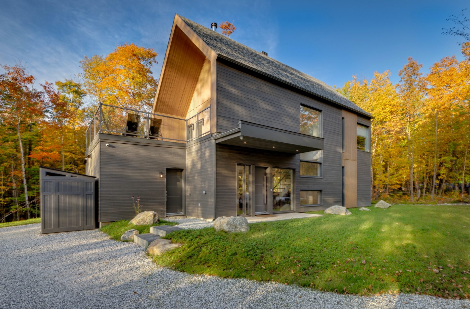 Maison scandinave sur dalle à 2 niveaux vue de l'extérieur. Revêtement extérieur gris et bois naturel, terrasse sur le garage